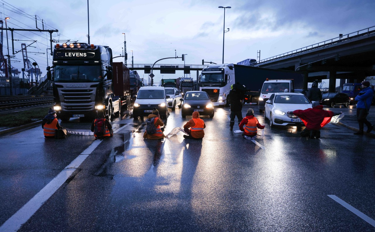 Demonstranten sitzen vor Pkw und Lkw im Hafen von Hamburg.