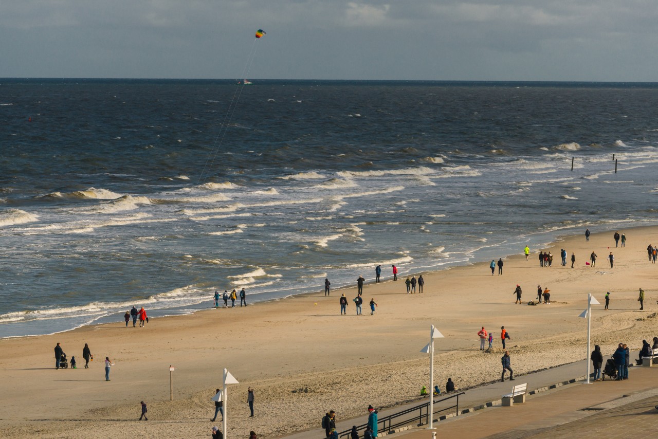 Menschen laufen am Strand auf Norderney entlang. 