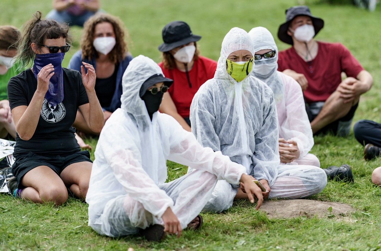 Klimaaktivisten in Schutzanzügen trainieren Verhalten bei Polizeimaßnahmen auf der Wiese eines Zeltcamps.