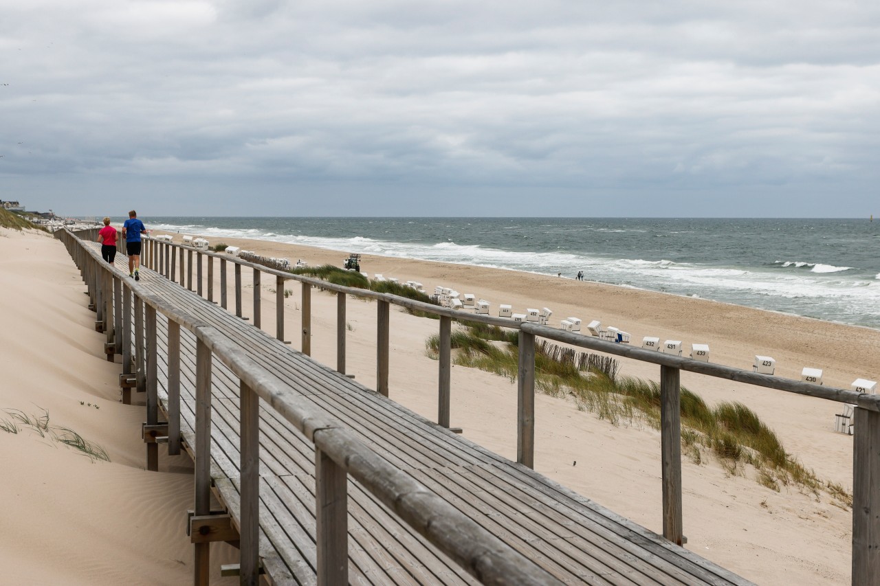 Sylt: Ein Mann und eine Frau joggen bei bewölktem Himmel am Strand von Westerland.