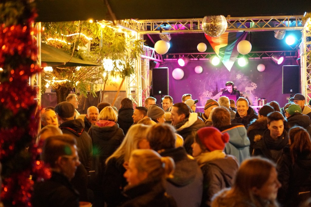 Menschen auf der Winter Pride, im Hintergrund ist große Bühne mit Diskokugel und LGBT-Flagge.