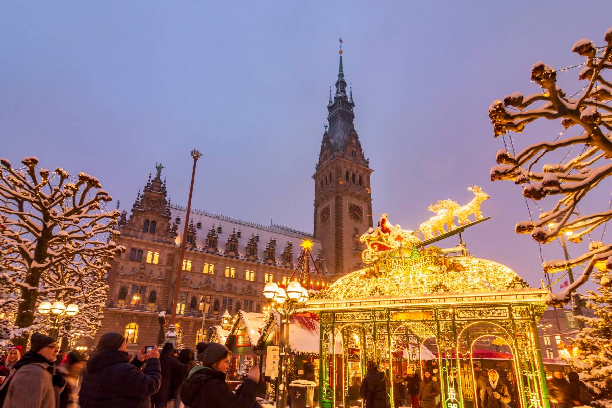 Leuchtender Weihnachtsmarkt mit Rathaus im Hintergrund.