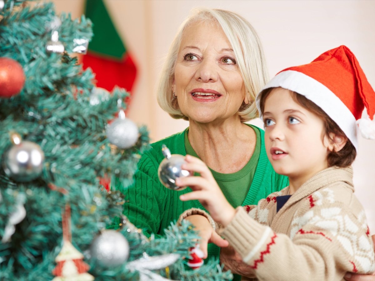 Ein kleiner Junge mit Weihnachtsmann-MÃ¼tze schmÃ¼ckt mit seiner Oma einen Weihnachtsbaum.